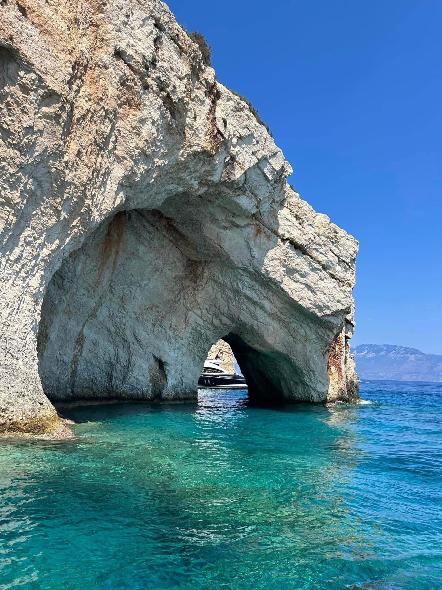 Dramatic rock arch framing turquoise water with a boat passing through