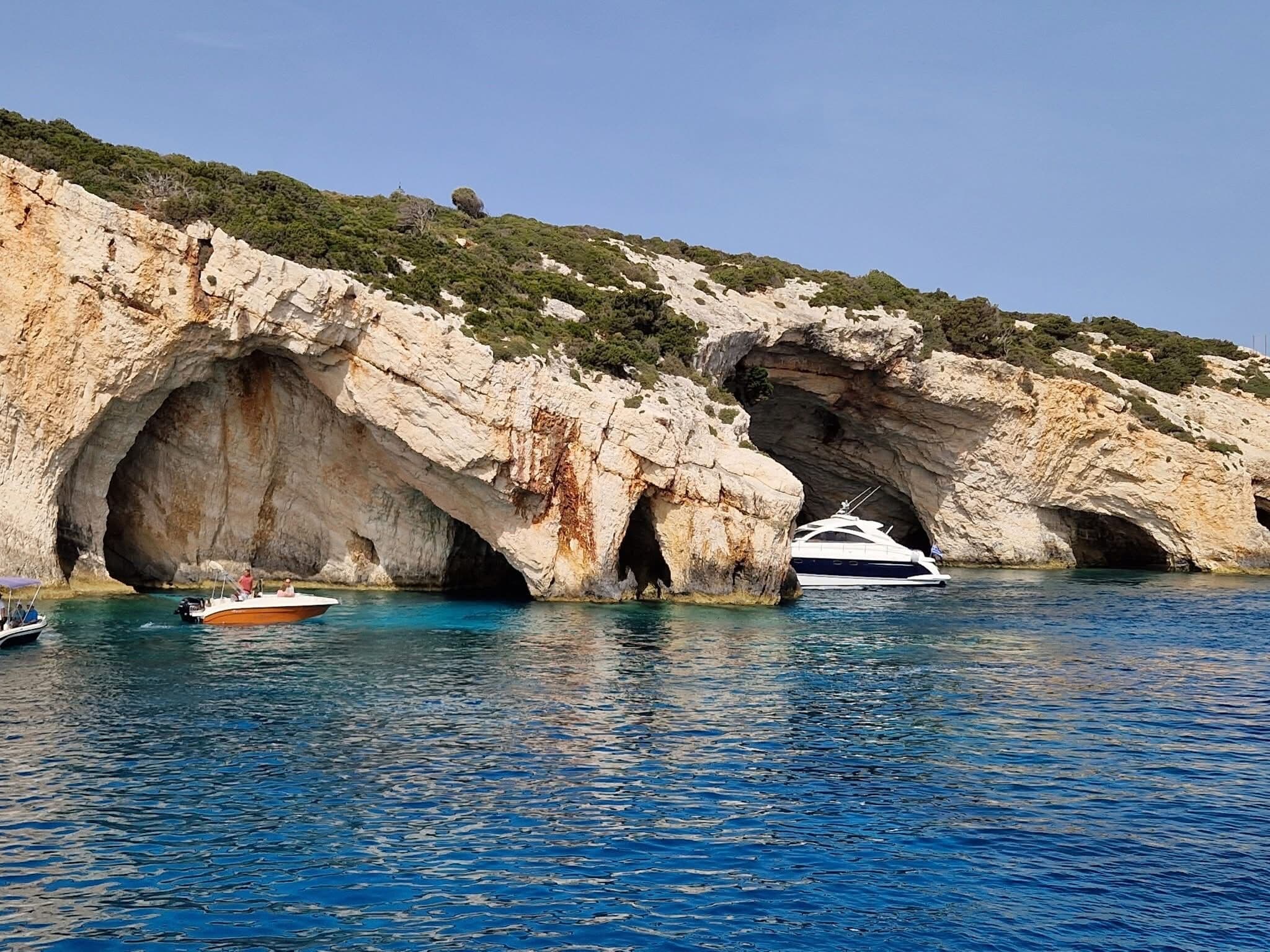 Boats arriving at the Blue Caves entrance with lush hillside above