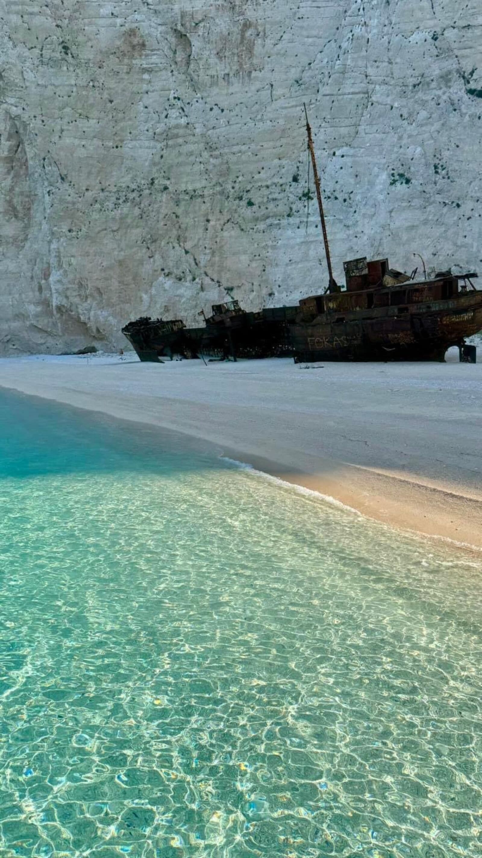 The shipwreck up close from the beach with towering cliffs behind