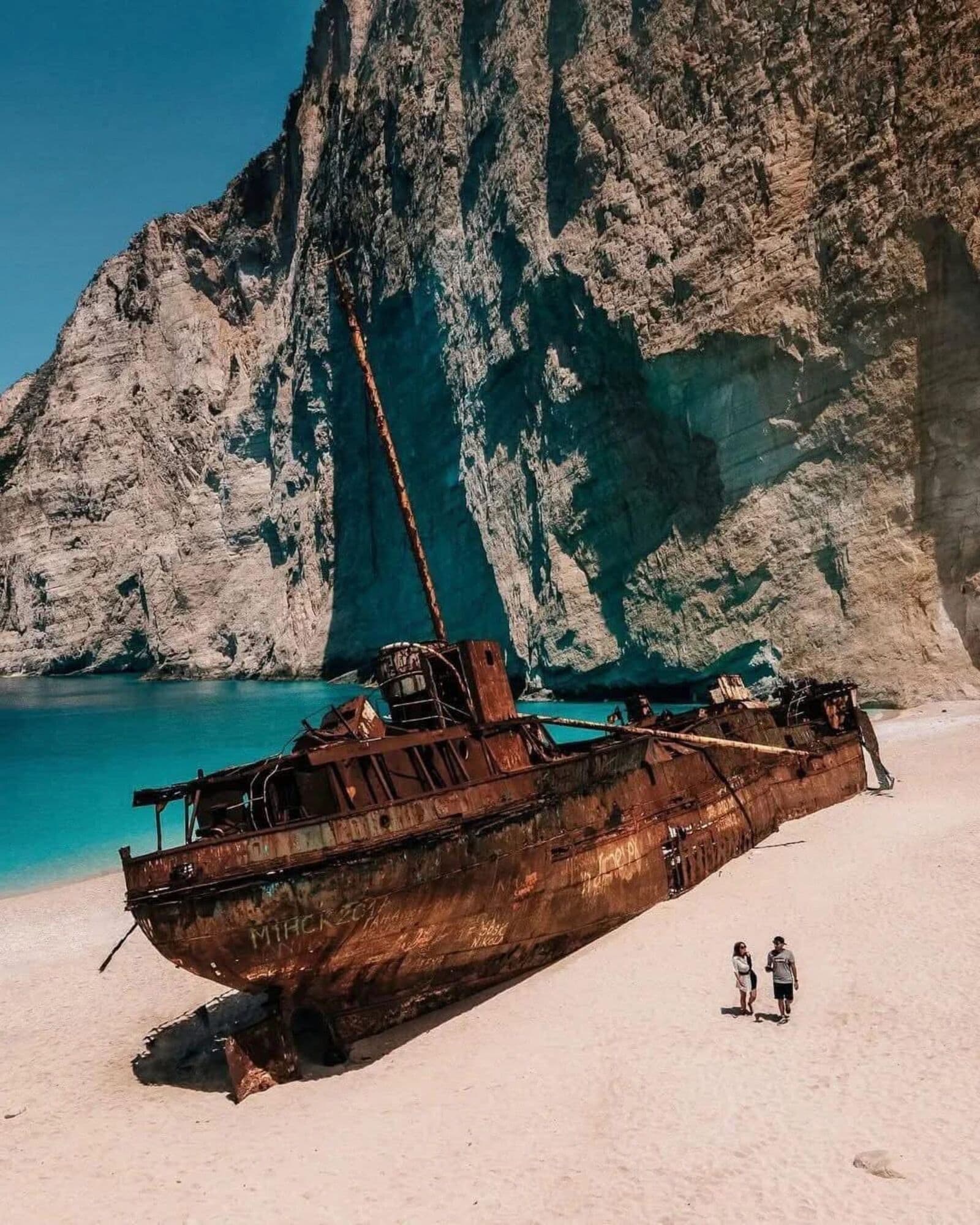 Visitors walking next to the shipwreck on the white sand